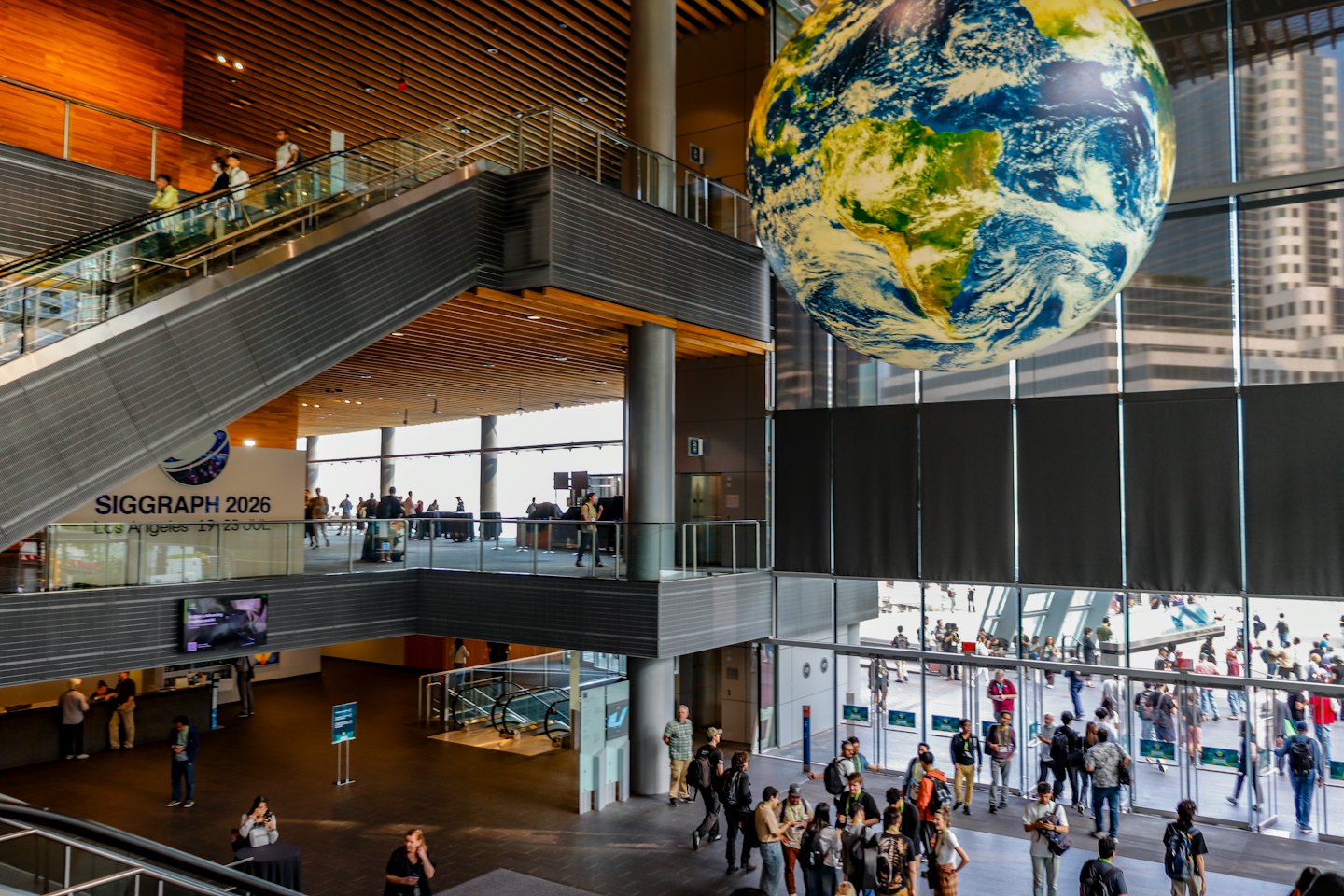 People walking through a large convention center beneath a hanging globe.