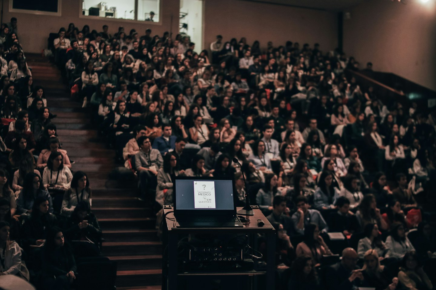 Audience watches a presentation on a laptop in a lecture hall.